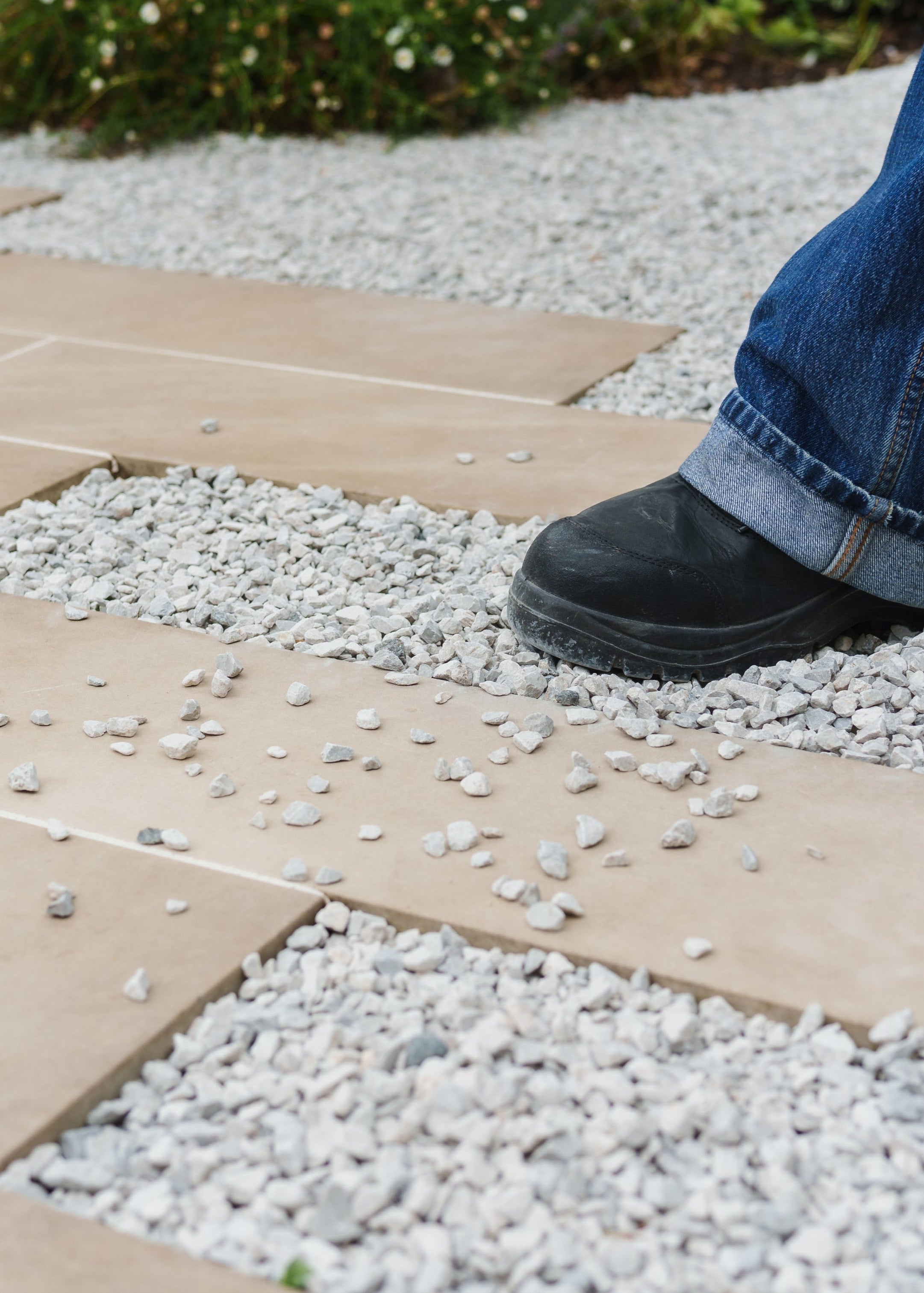 Person wearing blue jeans and black shoes stepping onto a stone patio from gravel