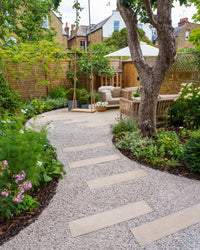 Backyard garden with a stone path, outdoor furniture, and greenery.