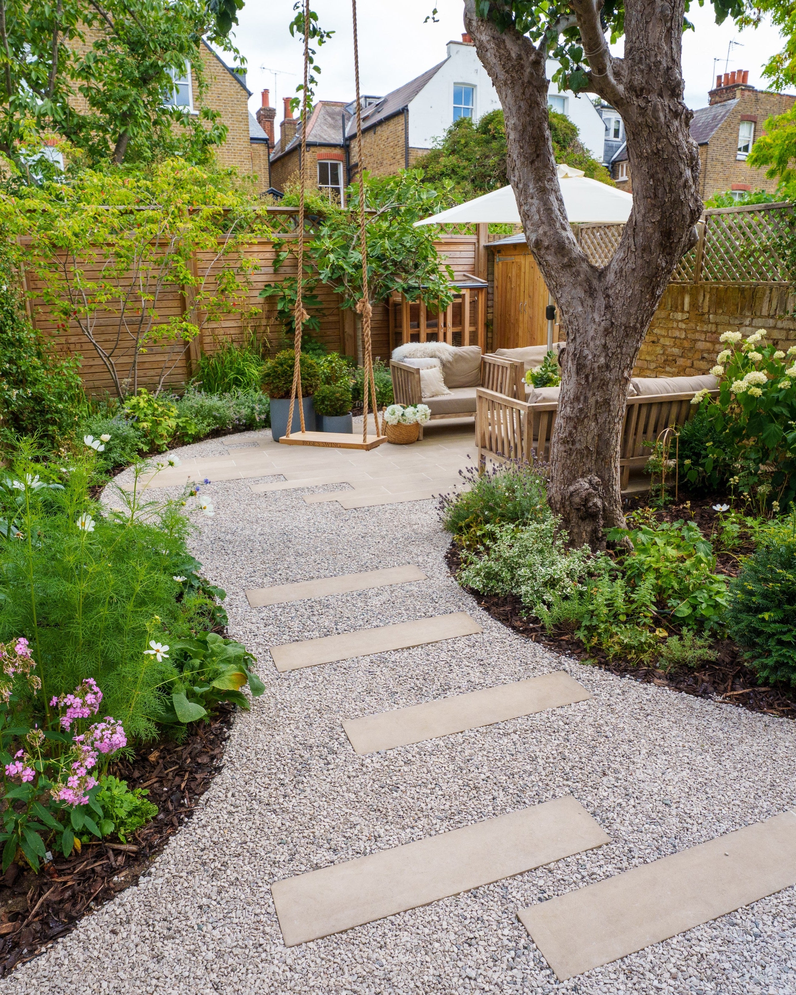 Backyard garden with a stone path, outdoor furniture, and greenery.
