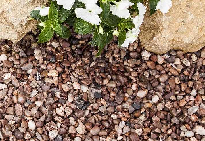 Pink and brown gravel laid next to rockery and white flowers