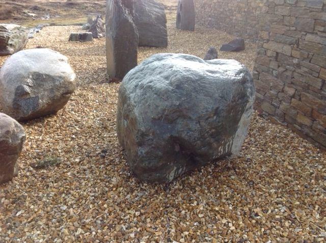 Wet single and dark welsh granite rockery boulder placed on golden gravel