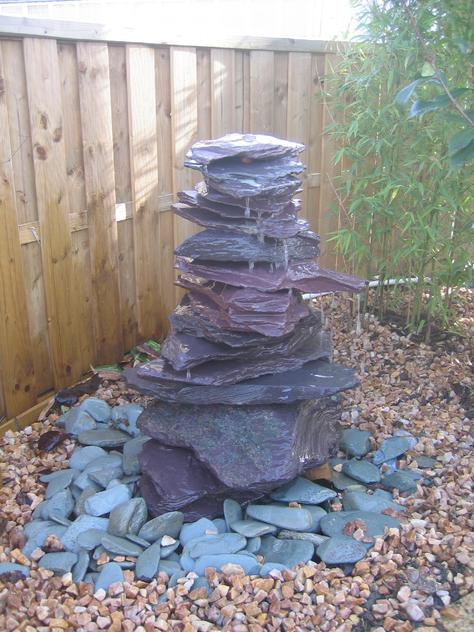 Plum and blue slate stones stacked for a water feature, paddlestones laid underneath alongside gravel chippings